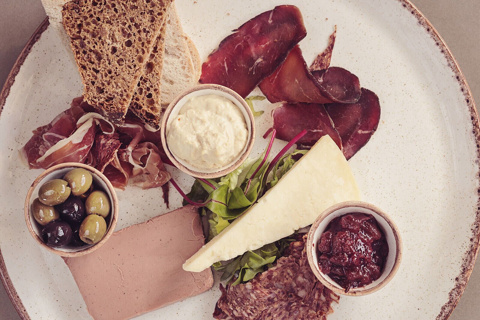 A charcuterie board with various meats, cheeses, olives, and bread.