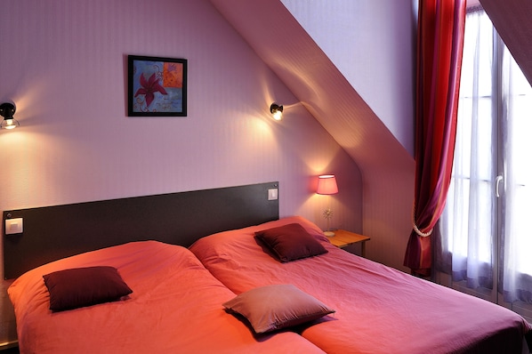Une chambre avec deux lits, un tableau au mur et une lampe sur une table de chevet.