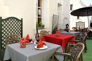 Un espace de restauration en plein air avec des tables disposées pour deux personnes, agrémenté de nappes rouges et de chaises en bois.