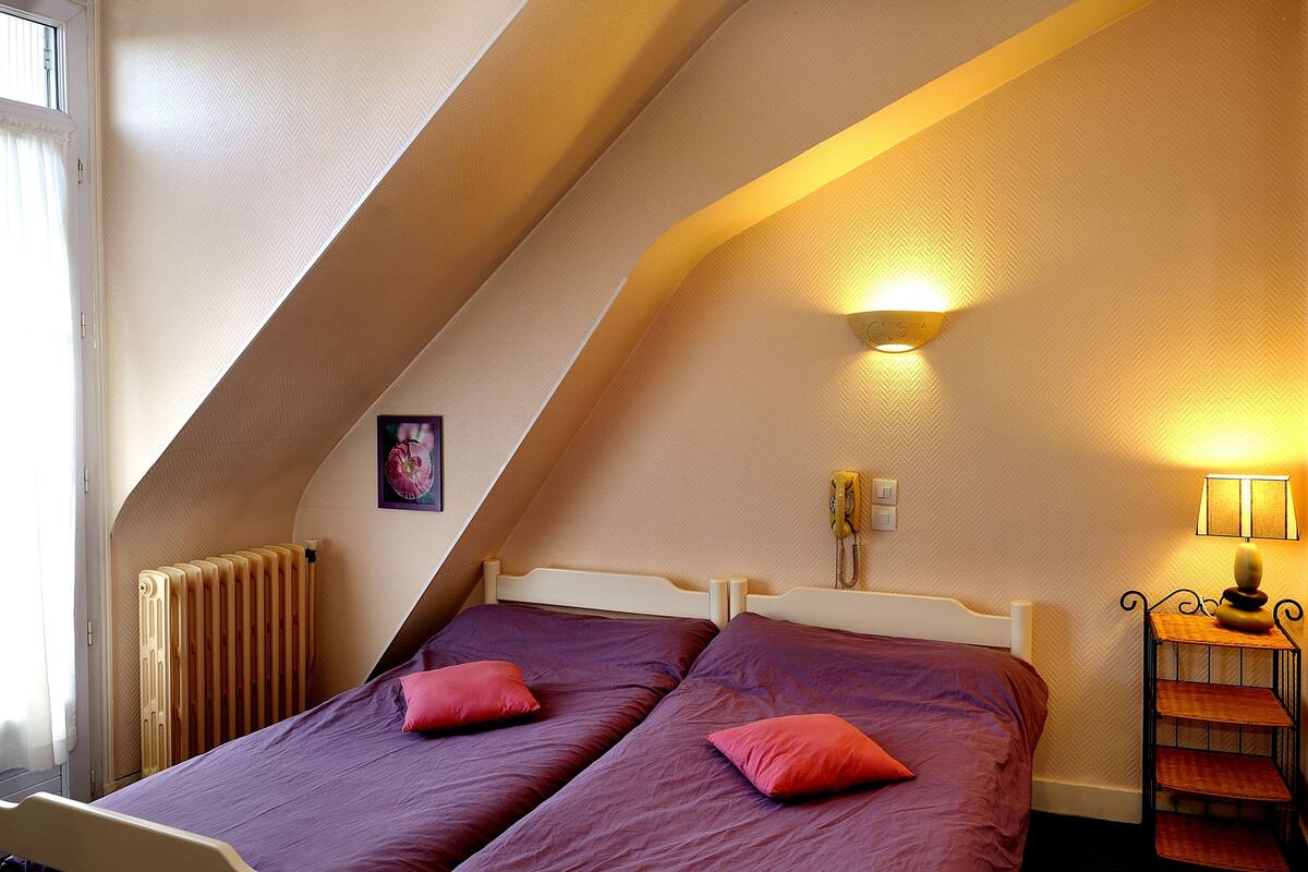 A bedroom with two beds, a radiator, a wall-mounted phone, and a bedside lamp.
