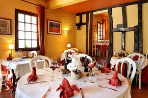 Un restaurant avec des tables rondes dressées pour le repas, agrémenté de chaises blanches et de serviettes rouges.