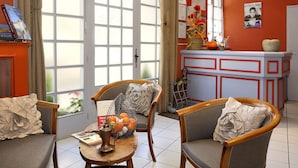 A room with a dining table, chairs, a basket of oranges, and a window with curtains. - Logis Auberge de la Treille (Saint-Martin-le-Beau)