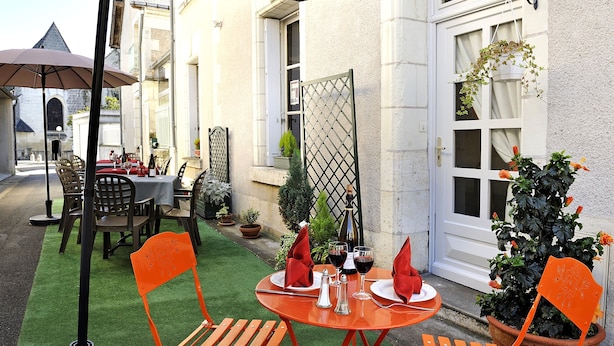 An outdoor dining area with tables and chairs, a potted plant, and a door. - Logis Auberge de la Treille (Saint-Martin-le-Beau)