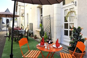Un espace extérieur aménagé pour les repas, avec des tables et des chaises, une plante en pot et une porte.