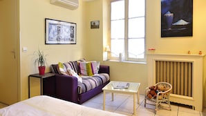 A room with a bed, a sofa, a chair, a table, a window, and a fireplace. - Logis Auberge de la Treille (Saint-Martin-le-Beau)
