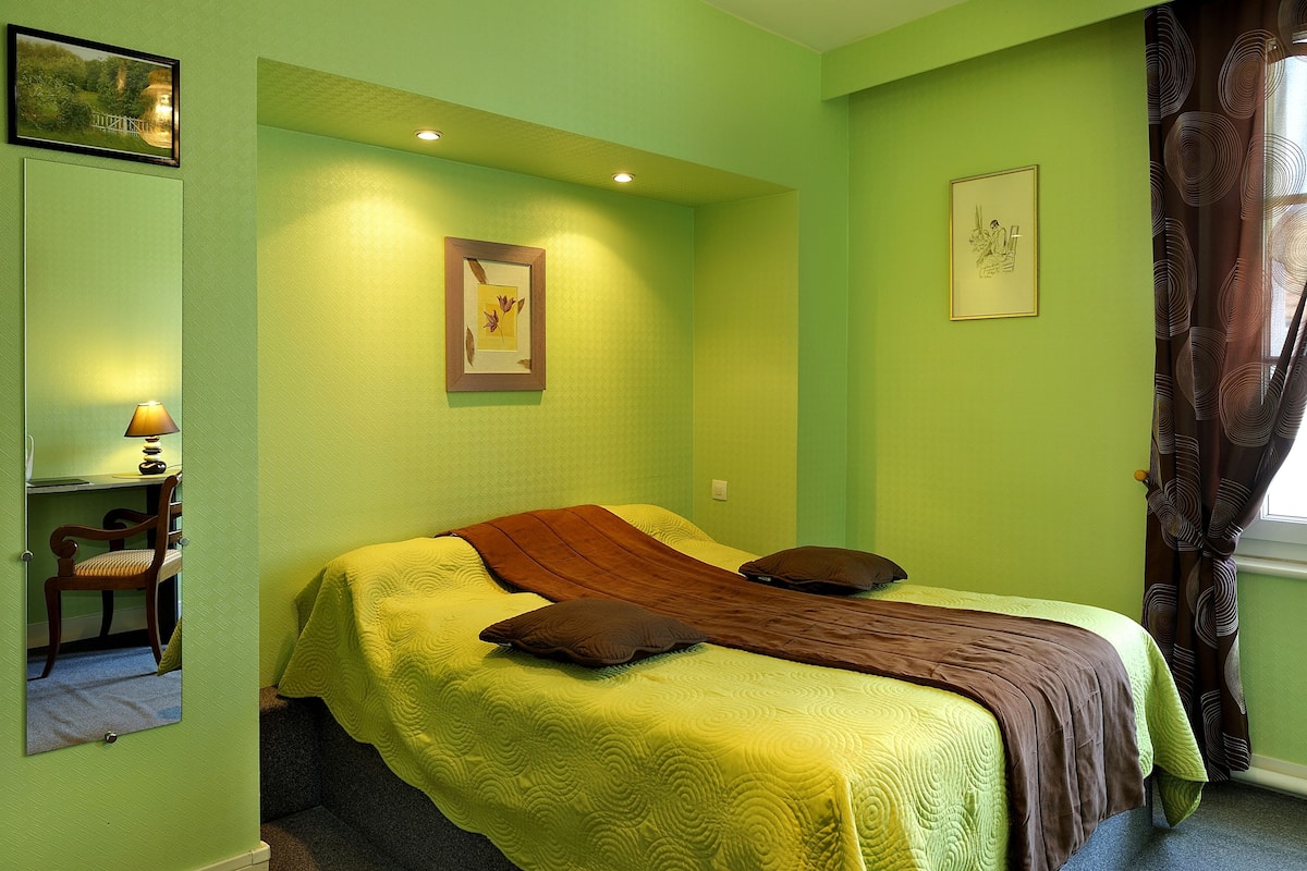 A room with a bed, a chair, a lamp, and two framed pictures on the wall.