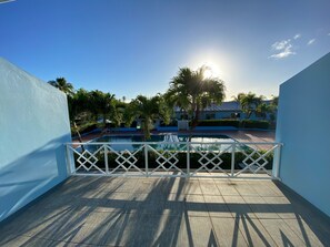 A pool area with a clear view of the pool, surrounded by palm trees and a blue building.