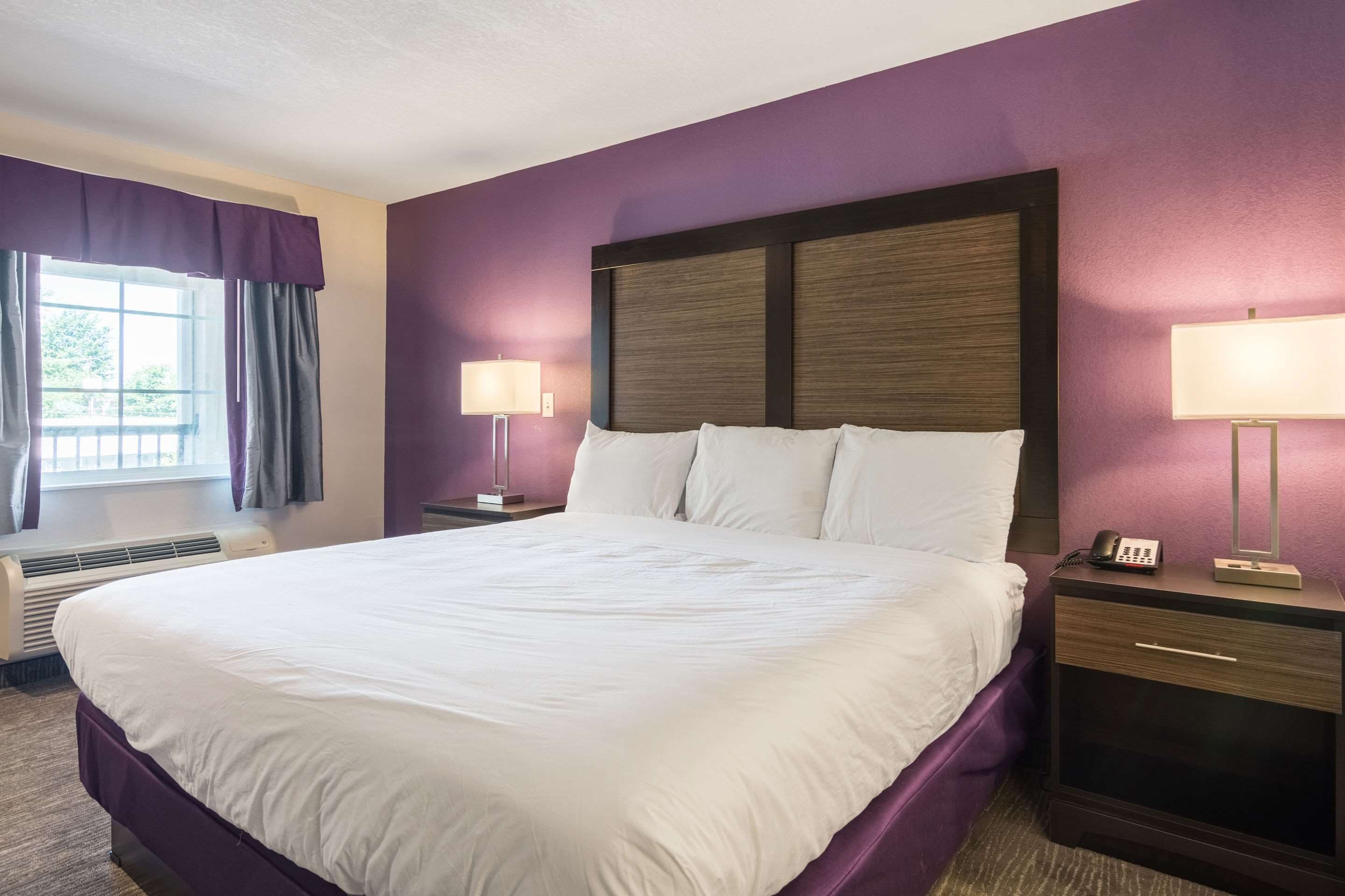 A hotel room with a large bed, two bedside lamps, a nightstand, and a window with curtains.