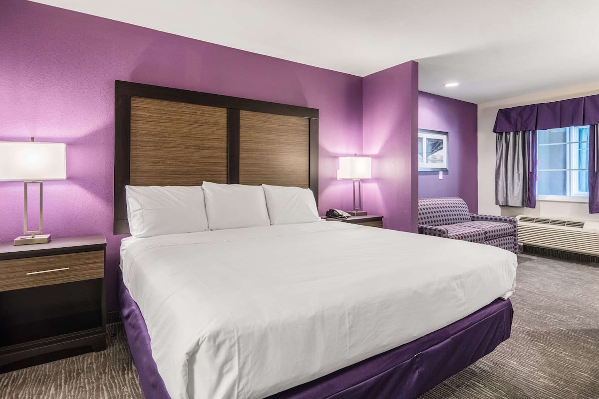 A hotel room with a large bed, two bedside tables, a chair, a window with curtains, and a wall-mounted phone.