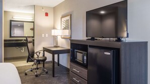 Una habitación de hotel con una cama, un escritorio con silla, televisión, microondas y refrigerador.
