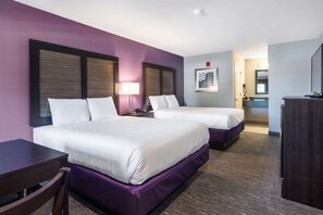 Habitación de hotel con dos camas, un escritorio, una silla, una lámpara, un baño con espejo y un televisor.