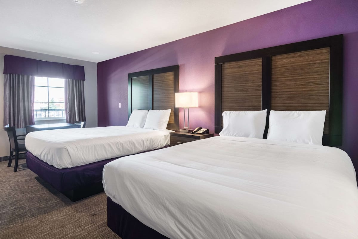 A hotel room with two beds, a desk, a chair, and a window with curtains.