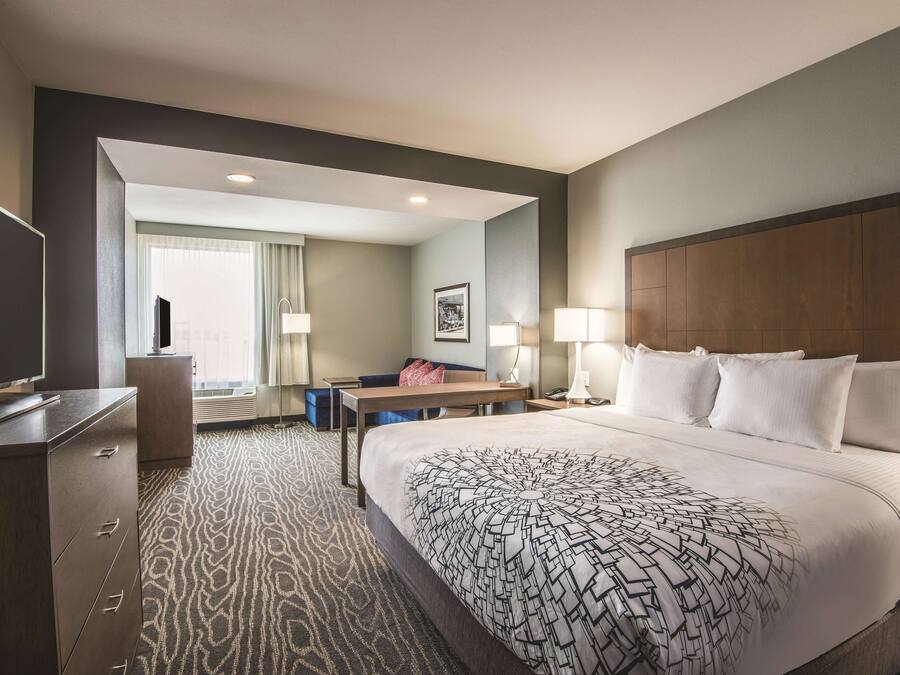 A hotel room with a large bed, a desk, a chair, a TV, and a window with curtains.