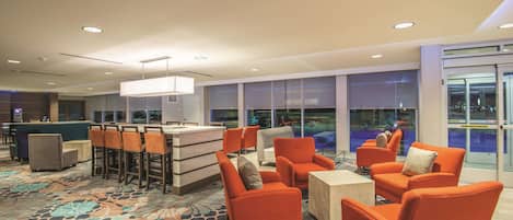 A hotel lobby with orange seating, a reception desk, and large windows offering a view of the outside.