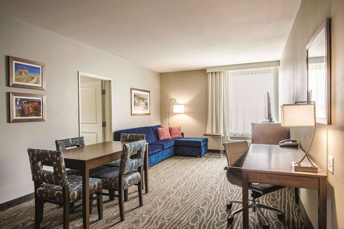 Una habitación de hotel con una mesa de comedor, sillas, un sofá, una lámpara y cuadros en la pared.