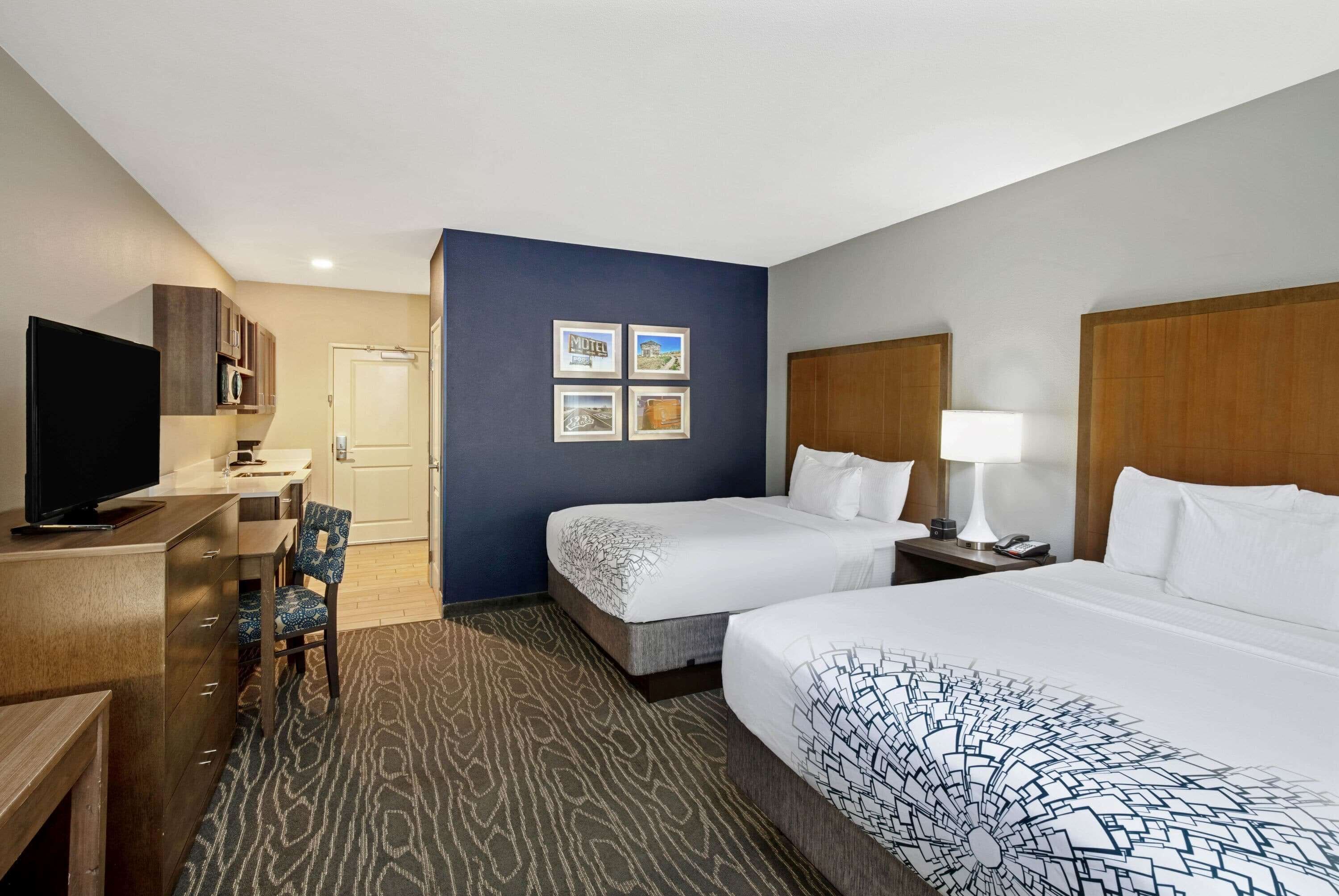 A hotel room with two beds, a desk with a television, a chair, and a microwave.