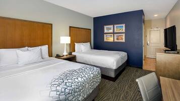 A hotel room with two beds, a desk, a chair, a TV, and a wall with framed pictures.