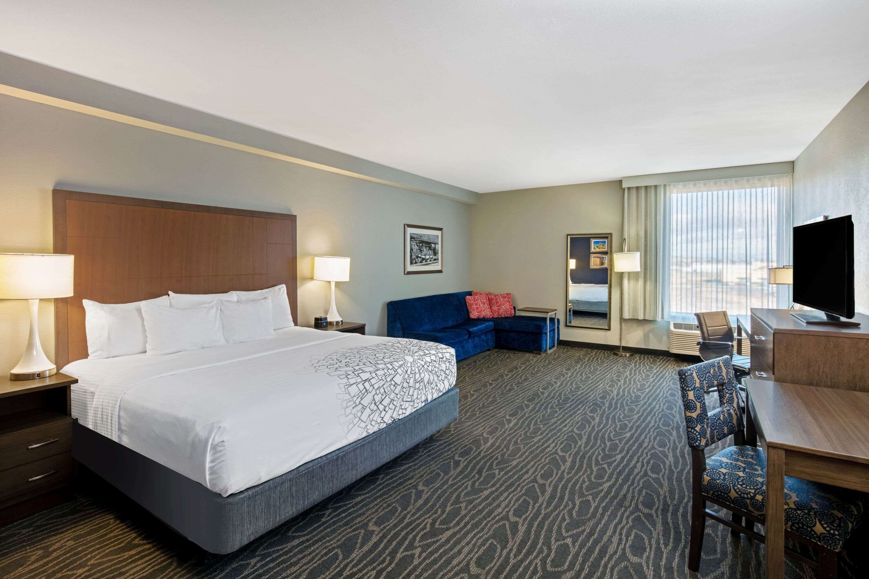 A hotel room with a large bed, a sofa, a desk, and a TV.