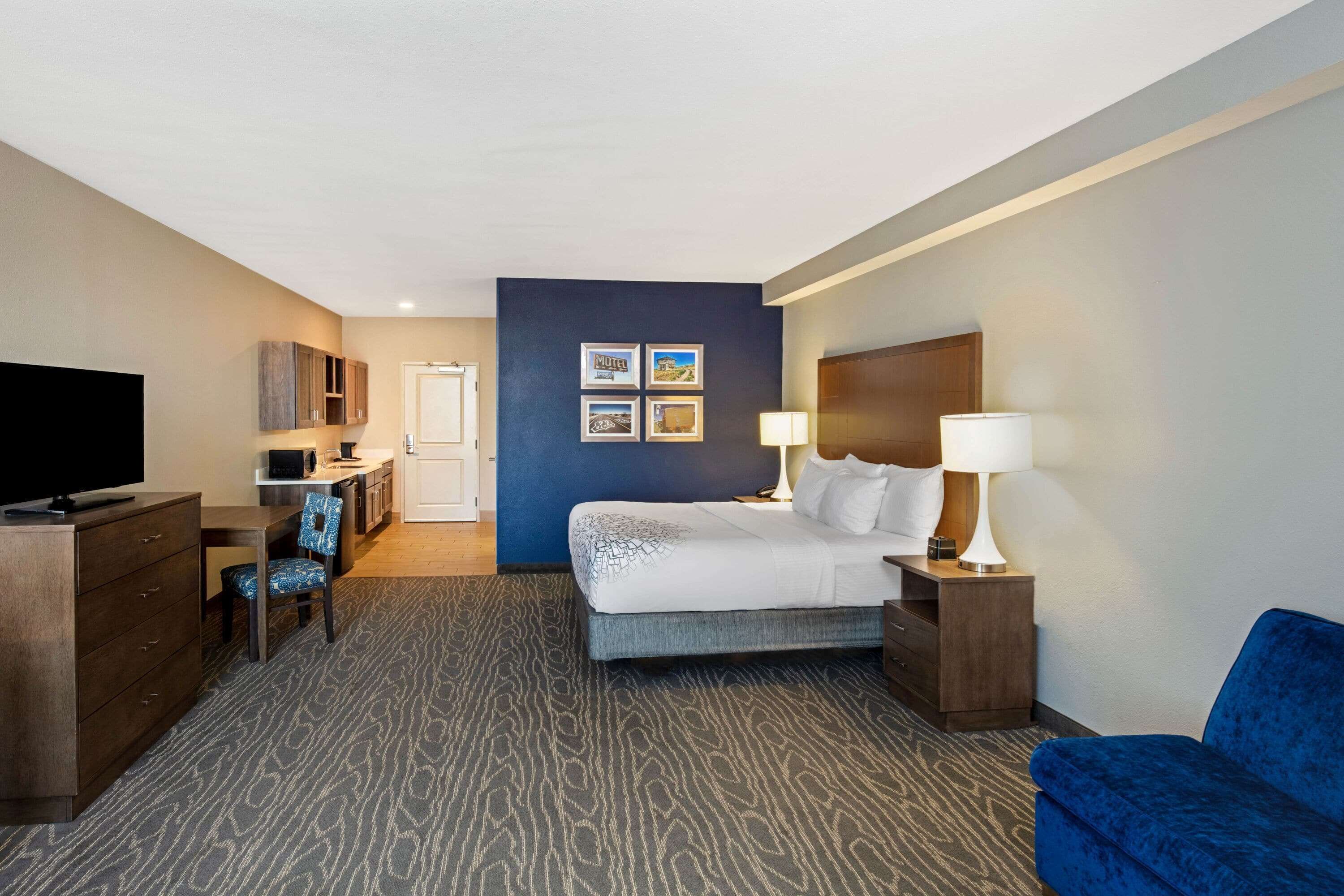 Una habitación de hotel con una cama, un escritorio con silla, un televisor, un aparador y un sillón azul.