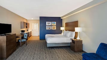 A hotel room with a bed, a desk with a chair, a television, a dresser, and a blue armchair.