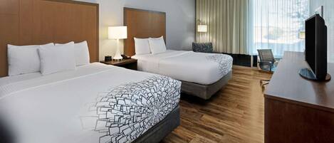 A hotel room with two beds, a desk with a television, and a window with curtains.