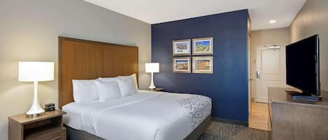 A hotel room with a large bed, two bedside tables with lamps, a flat-screen TV, and a door leading to a bathroom.
