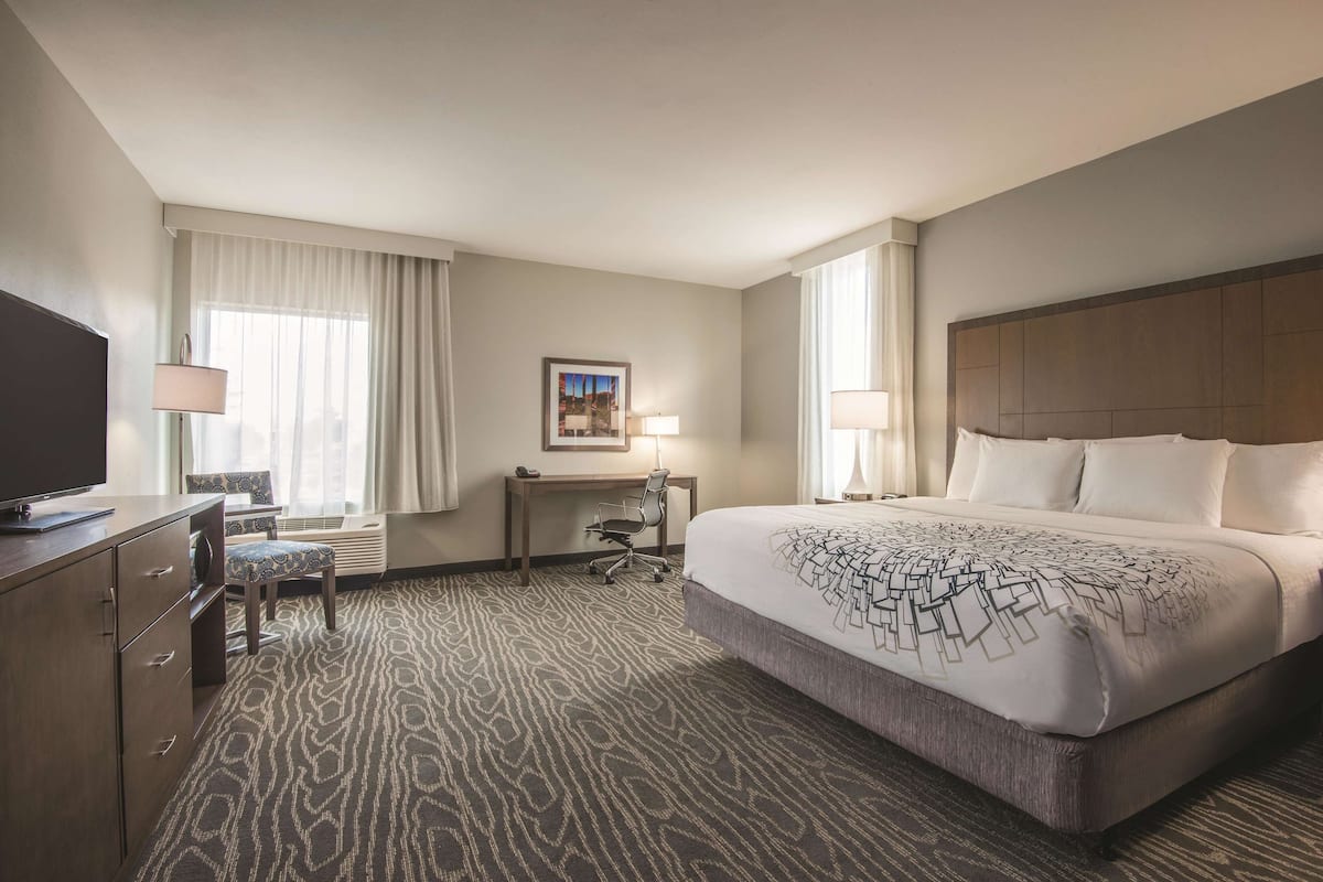 Una habitación de hotel con una cama grande, un escritorio con silla, televisión y ventana con cortinas.