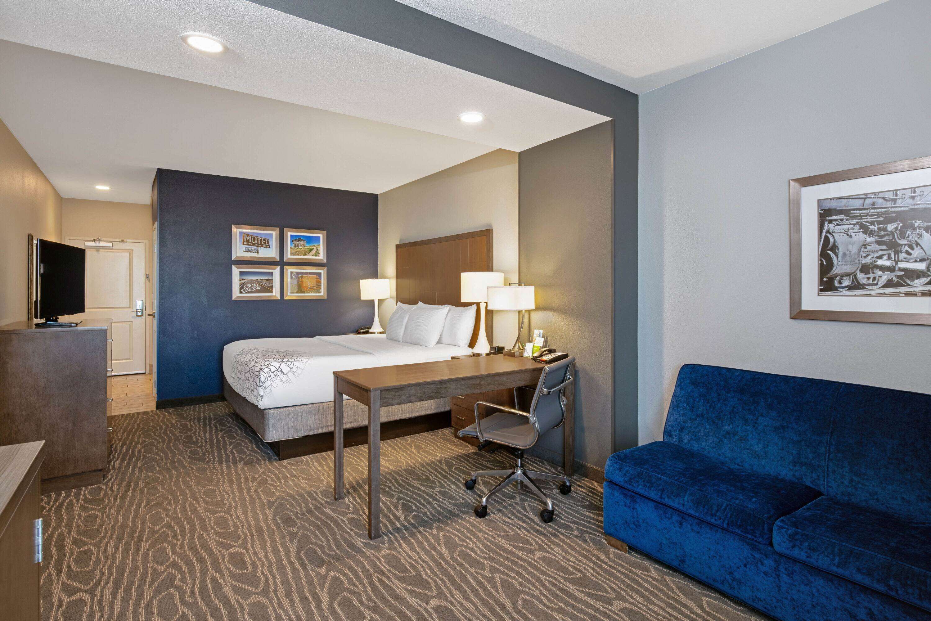 Una habitación de hotel con cama, escritorio, silla y sofá azul.