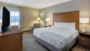 A hotel room with a large bed, a television on a desk, two bedside lamps, a chair, and a window with curtains.