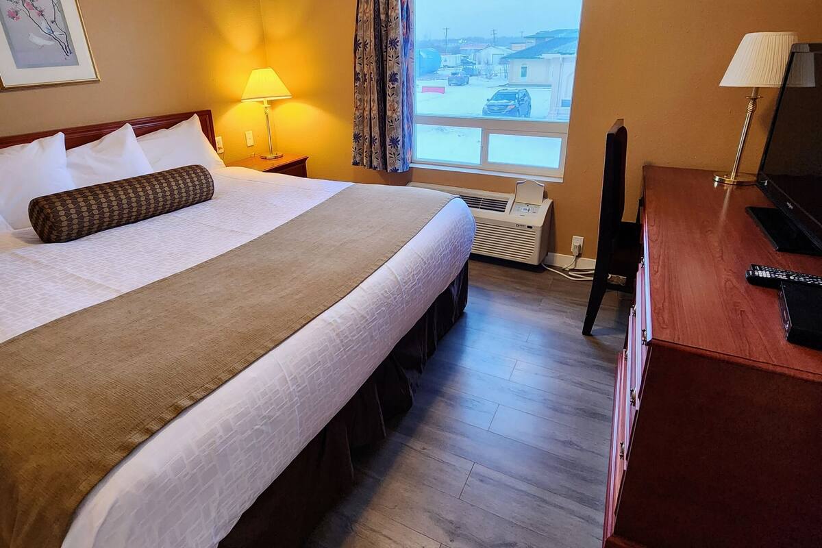 Una habitació d'hotel amb un llit gran, una taula de treball, una cadira, una làmpada, una finestra amb vistes i una làmpada al sostre.