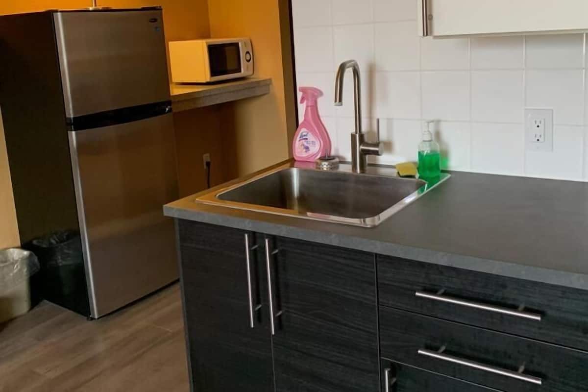 Una cuina moderna amb armaris foscos, un obrador d'acer inoxidable, un microones i un frigorífic.