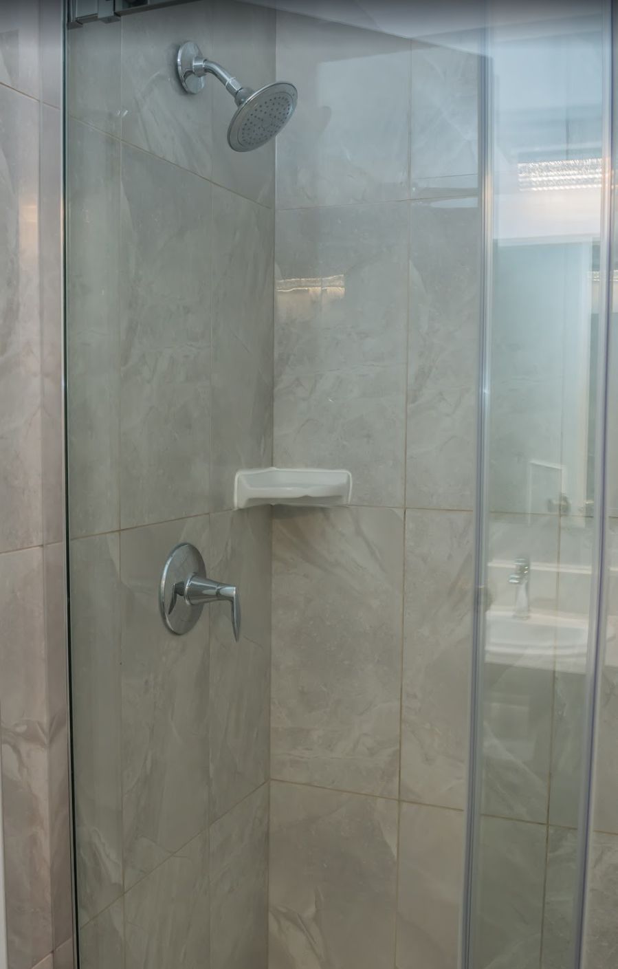 A glass-enclosed shower with a handheld showerhead and a wall-mounted control.