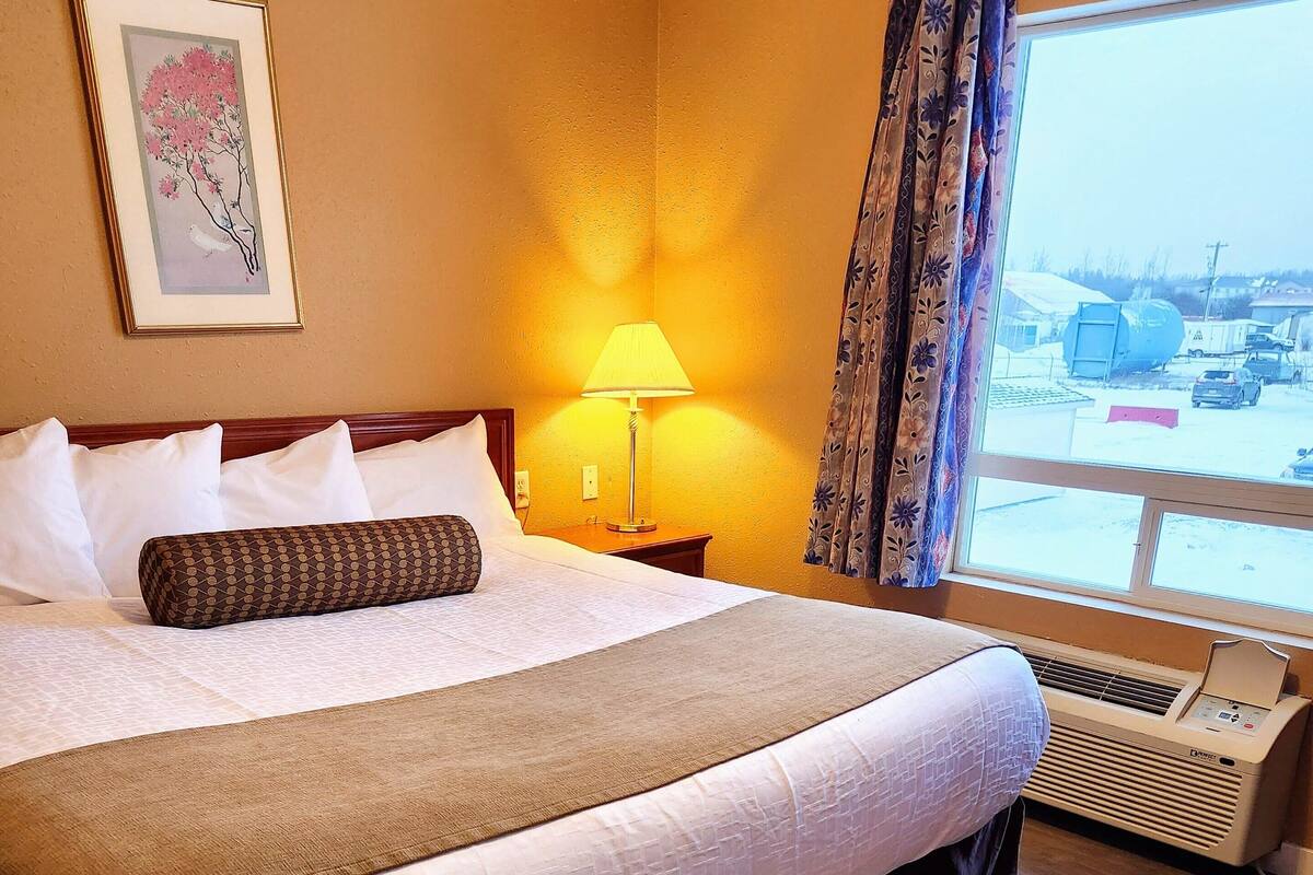 Una habitació d'hotel amb un llit gran, una làmpada de nit, una finestra amb cortines i un quadre al mur.