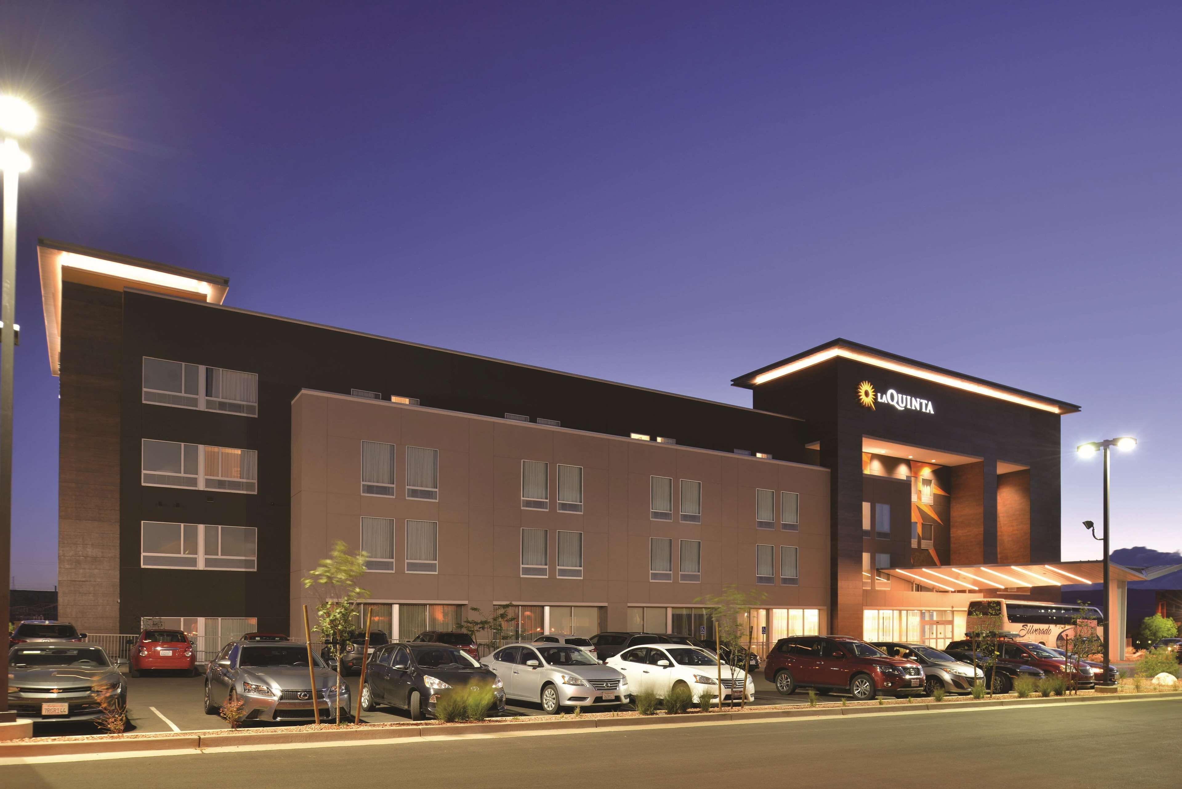 A hotel with a modern design, featuring a parking lot with several cars and a well-lit entrance.