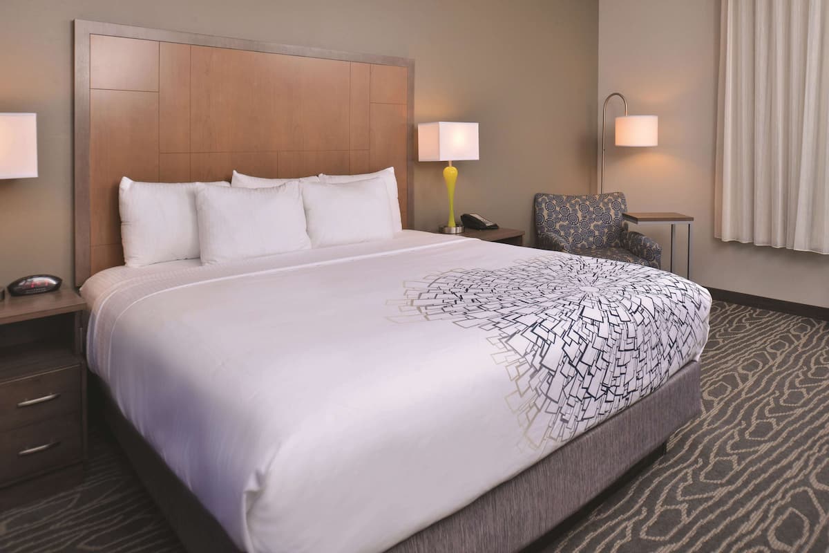A hotel room with a large bed, two bedside lamps, a chair, a small table, and a telephone.