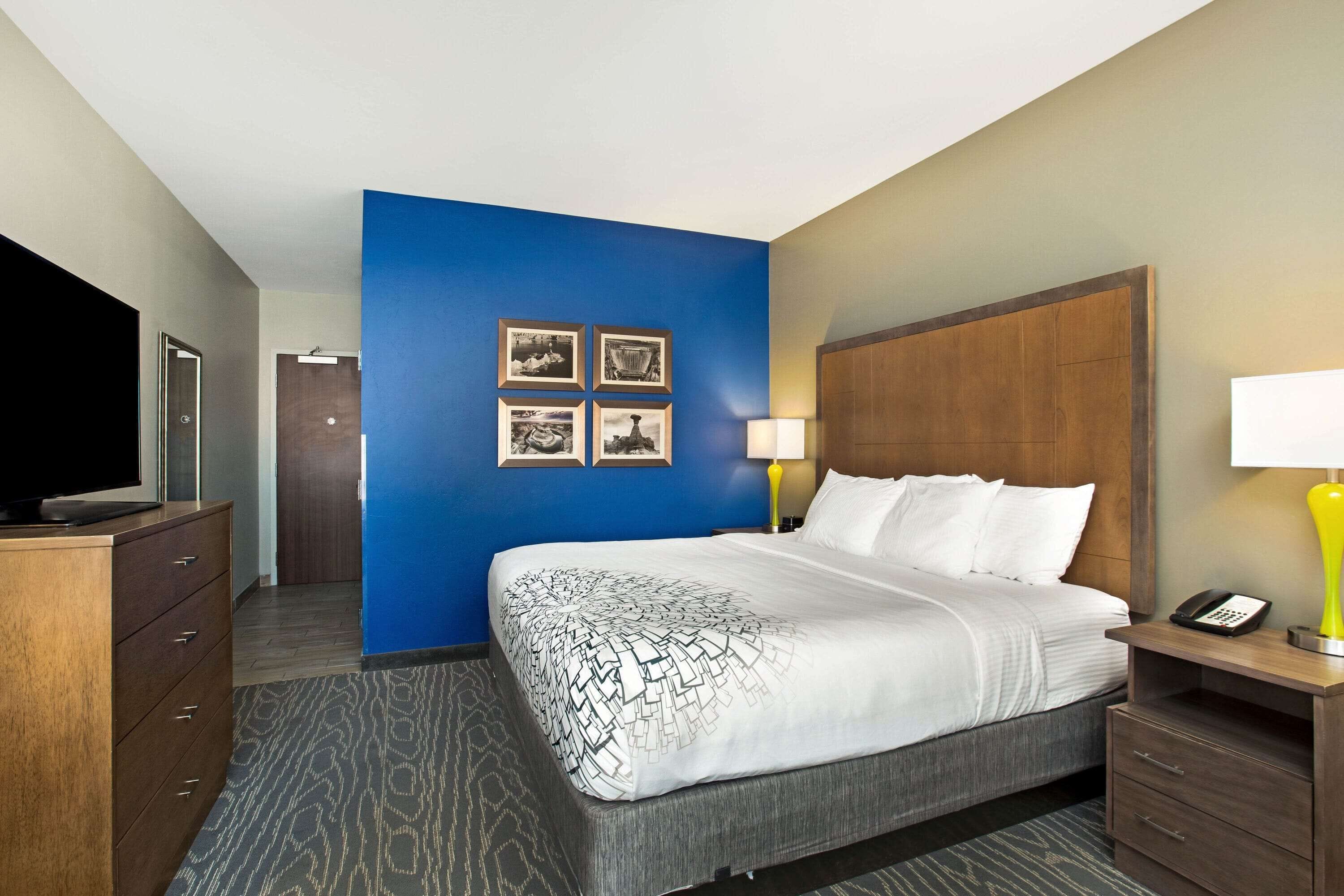 A hotel room with a large bed, a television, a desk with a lamp, and a wooden headboard.
