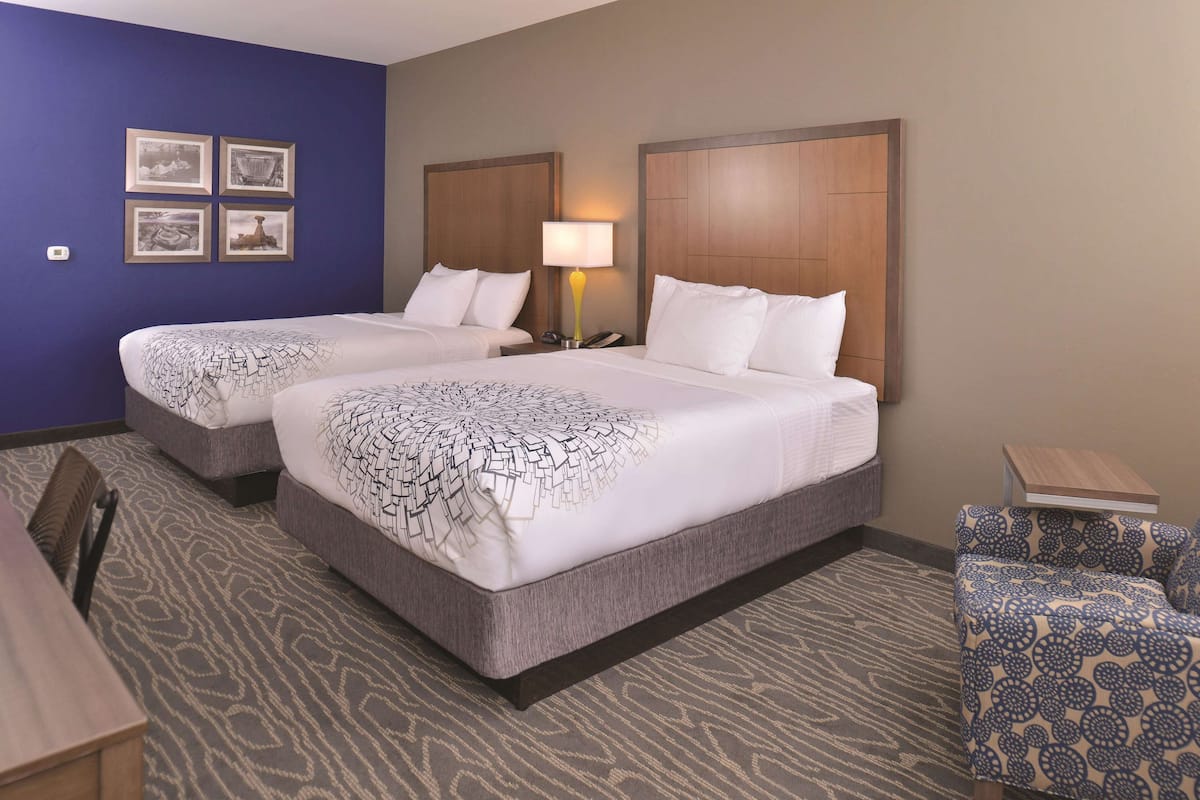 A hotel room with two beds, a desk, a chair, and a small table.