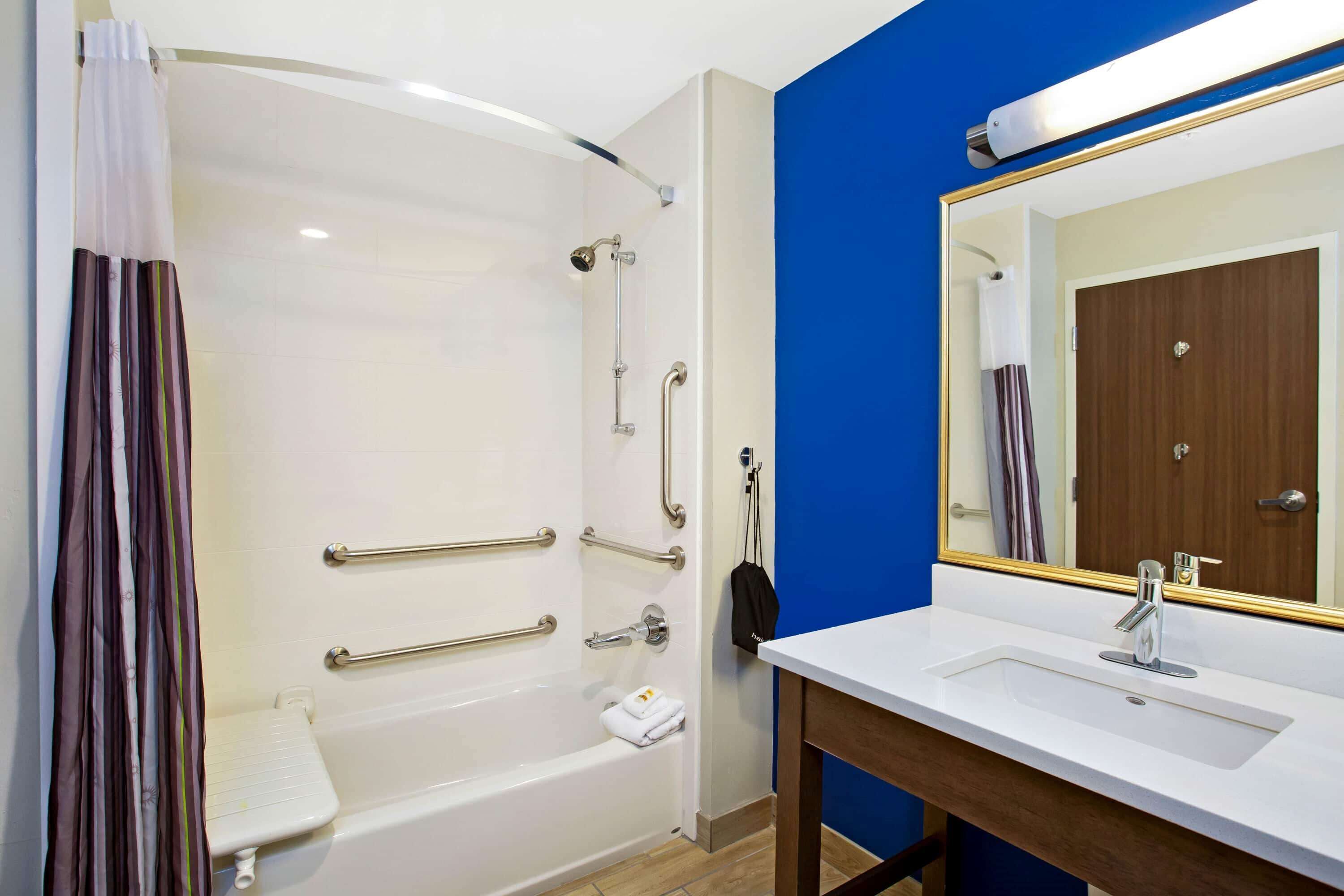 A bathroom with a white bathtub, a sink with a mirror, and a shower with grab bars.