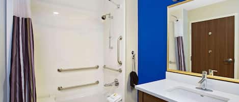 A bathroom with a white bathtub, a sink with a mirror, and a shower with grab bars.