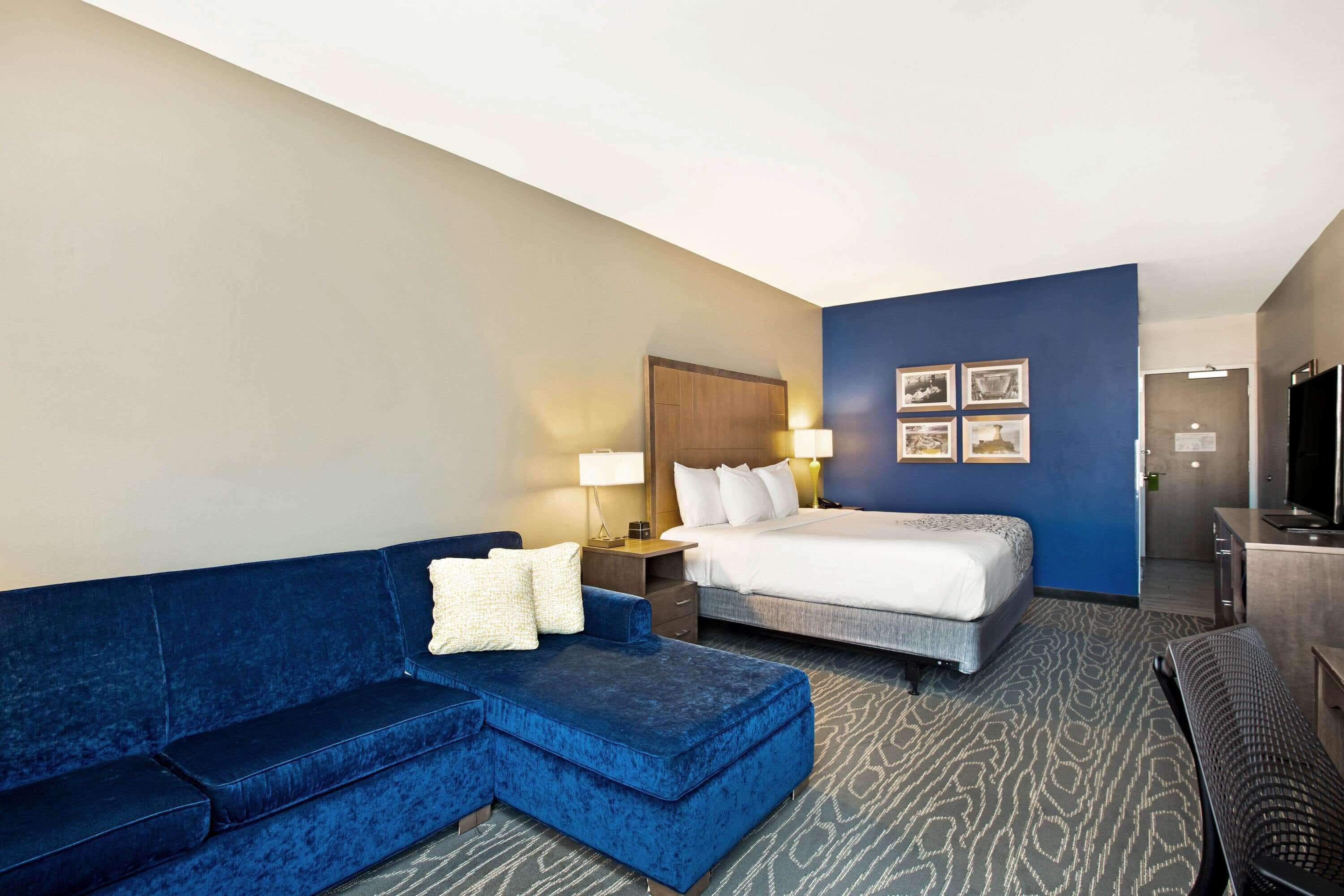 Una habitación de hotel con un sofá azul, una cama, un escritorio y un televisor.