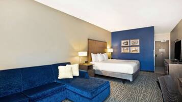 Una habitación de hotel con un sofá azul, una cama, un escritorio y un televisor.