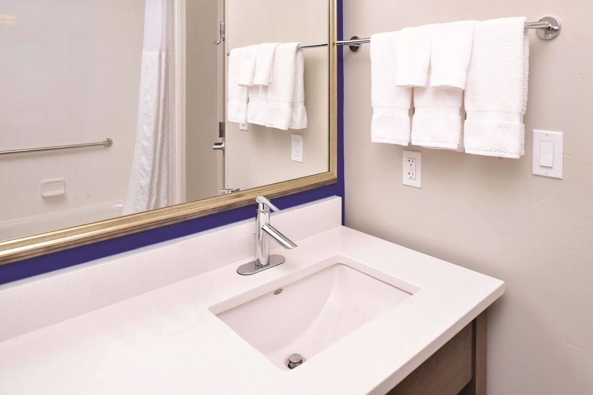 A bathroom with a white sink, a mirror with a gold frame, and two white towels hanging on a towel bar.