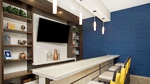 A modern interior with a long counter, seating area, and a large flat-screen TV mounted on the wall. - La Quinta Inn & Suites by Wyndham Page at Lake Powell (Page)