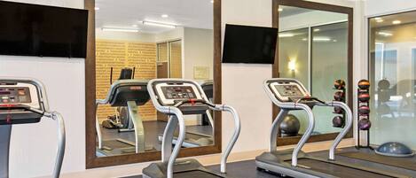 Three treadmills in a gym with mirrors on the walls and a television mounted above one of the mirrors.