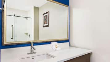 Un baño con lavamanos blanco, un espejo grande con marco dorado y dispensador de toallas.