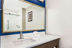 Un baño con lavamanos blanco, un espejo grande con marco dorado y dispensador de toallas.