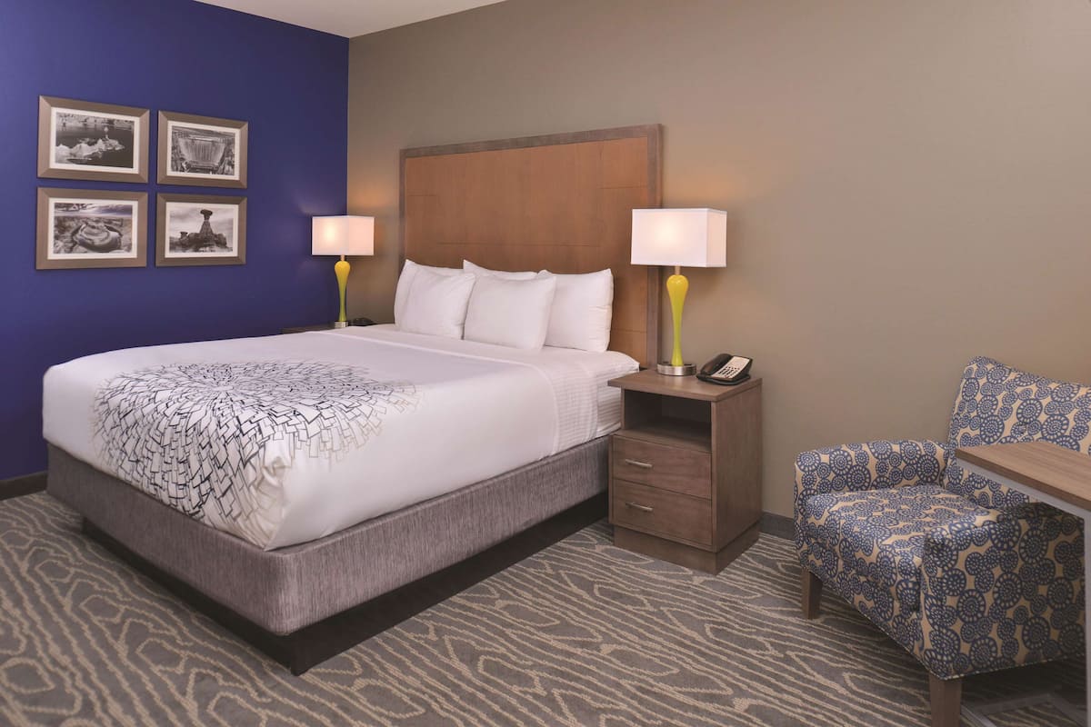 A hotel room with a large bed, bedside tables with lamps, a chair, and framed pictures on the wall.
