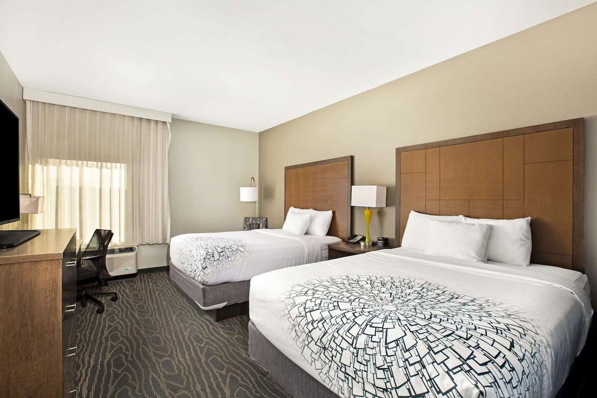 A hotel room with two beds, a desk, a TV, and a window with curtains.