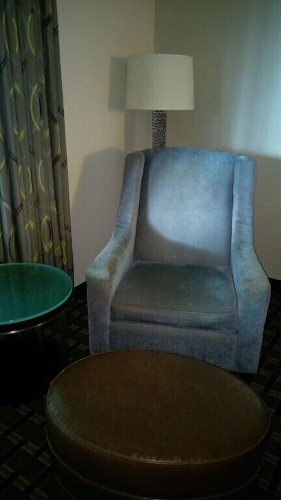 Una habitación con un sillón azul y un otoman redondo.
