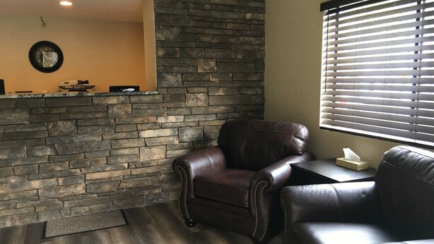 Zona de recepción con pared de piedra, sillones de cuero, un reloj y una ventana con persianas.